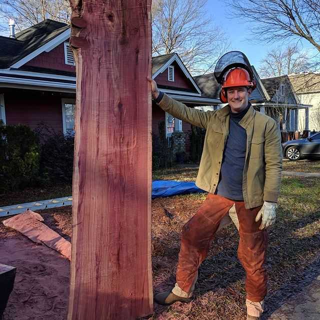 A man in a helmet holds a red cedar slab